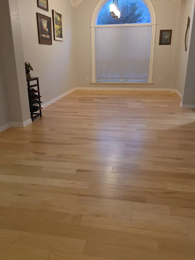 An empty room with a new oak floor running to an arched window